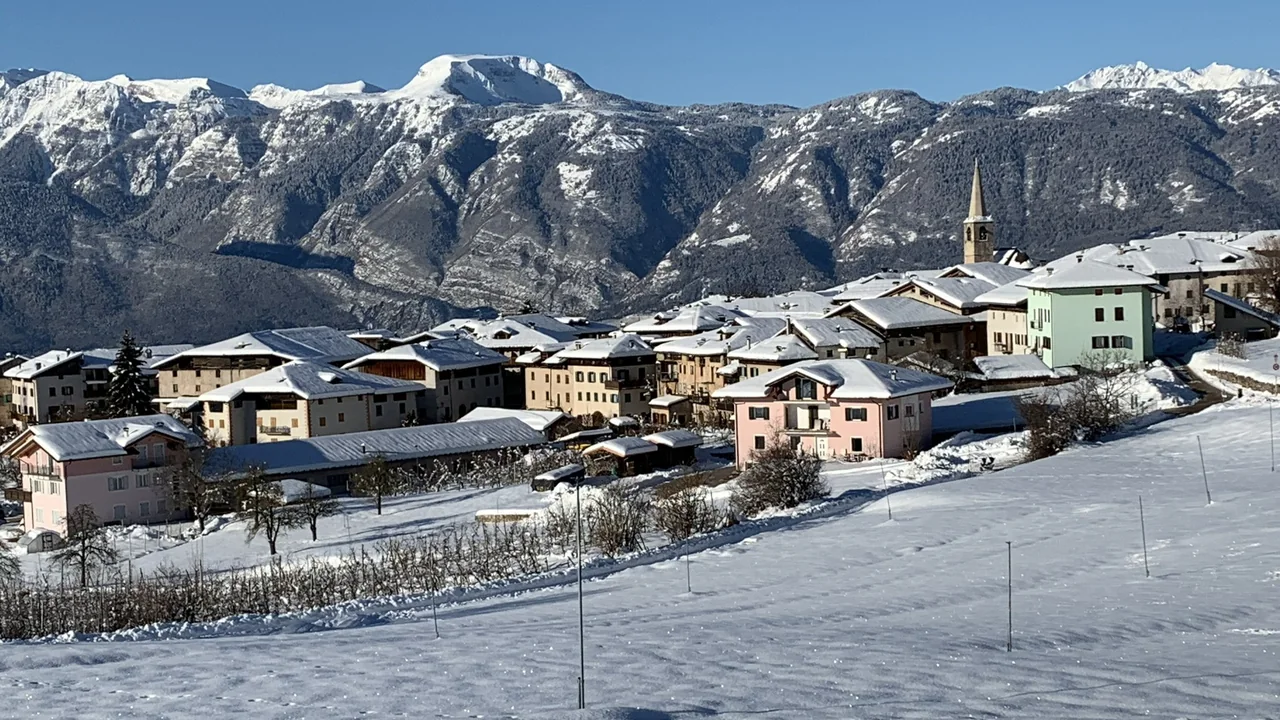 Borgo innevato con campanile e montagne sullo sfondo
